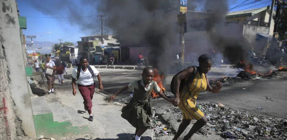 Una mujer y su hija pasan corriendo frente a una barricada levantada por la policía en protesta por el mal gobierno policial en Puerto Príncipe, Haití, el 26 de enero de 2023. Las casi 200 pandillas de Haití se han aprovechado del caos, luchando por el control.  AP