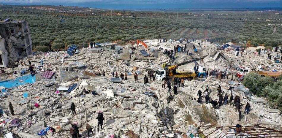 Esta vista aérea muestra a los residentes, ayudados por equipos pesados, buscando víctimas y supervivientes entre los escombros de los edificios derrumbados tras un terremoto en el pueblo de Besnia, cerca de la localidad de Harim, en la provincia siria de Idlib, controlada por los rebeldes, en la frontera con Turquía, el 6 de febrero de 2022. Fuente: AFP.
