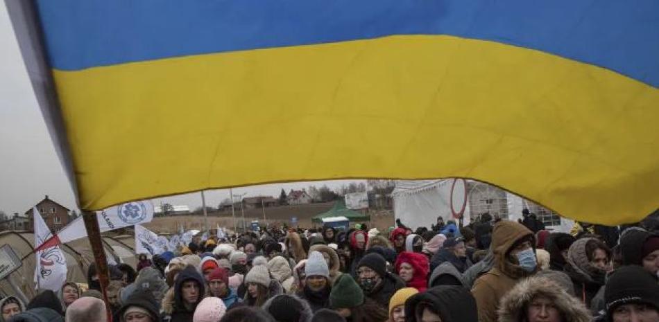 El voluntario ucraniano Oleksandr Osetynskyi, de 44 años, sostiene una bandera ucraniana y dirige a cientos de refugiados tras huir de Ucrania y llegar al cruce fronterizo en Medyka, Polonia, el lunes 7 de marzo de 2022. La guerra ha sido una catástrofe para Ucrania y desencadenado una crisis para todo el planeta. (AP Foto)