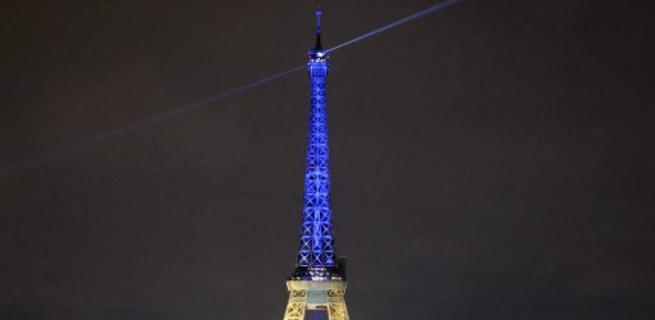 Los transeúntes observan la Torre Eiffel iluminada con los colores de la bandera ucraniana en una muestra de apoyo a Ucrania, un año después de que Rusia lanzara una invasión militar en el país, en París el 23 de febrero de 2023.  Ludovico MARIN / AFP