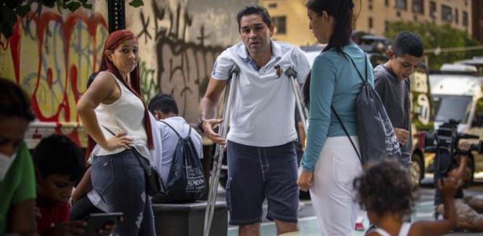 Eduardo García, de Venezuela, con muletas, y rodeado de su familia afuera de la sede de Caridades Católicas, el 16 de agosto de 2022 en Nueva York. AP