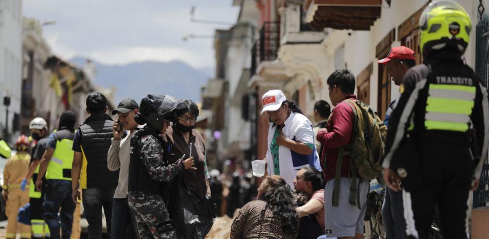 La policía habla con las personas junto al sitio donde un automóvil fue aplastado por los escombros después de un terremoto que sacudió Cuenca, Ecuador, el sábado 18 de marzo de 2023.