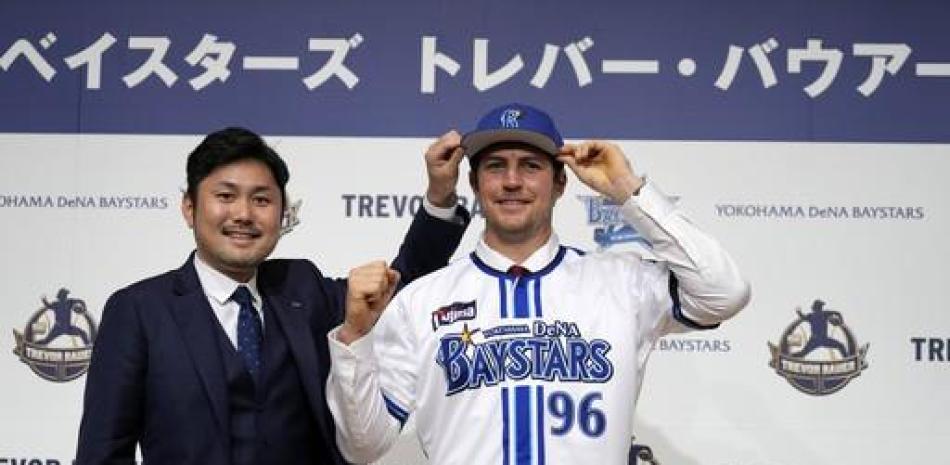 Trevor Bauer porta el uniforme y gorra del Yokohama DeNA BayStars junto al director de operaciones del equipo Tatsuhiro Hagiwara en la conferencia de prensa.