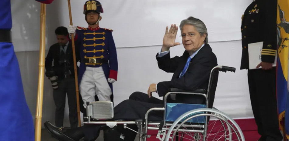 El presidente de Ecuador, Guillermo Lasso, en silla de ruedas, saluda a la prensa mientras espera al mandatario de República Dominicana, Luis Abinader, en el palacio de gobierno antes de la reunión de la Alianza para el Desarrollo en Democracia, en Quito, Ecuador, el lunes 6 de marzo de 2023. La Corte Constitucional de Ecuador avaló el miércoles 29 de marzo de 2023 el inicio de juicio político contra el presidente Lasso ante la Asamblea Nacional, presentado por la oposición en busca de la destitución presidencial. (AP Foto/Dolores Ochoa