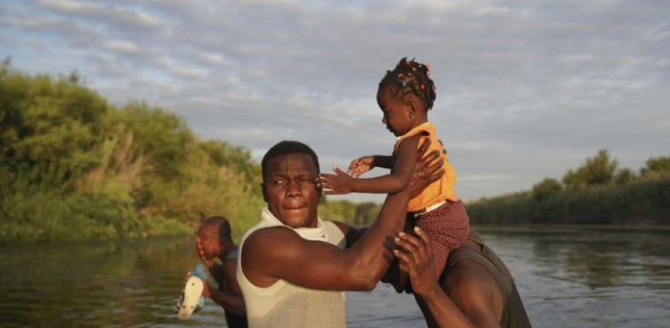Hombres cargan a una niña a través del Río Bravo mientras los migrantes, muchos de Haití, abandonan Del Río, Texas, para regresar a Ciudad Acuña, México, el miércoles 22 de septiembre de 2021 temprano, algunos para evitar una posible deportación de EEUU otros a conseguir suministros. (AP Foto/Fernando Llano)