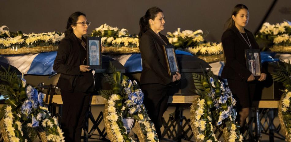 Oficiales de la Cancillería sostienen retratos junto a los ataúdes de los migrantes guatemaltecos cuyos restos llegaron a la Base de la Fuerza Aérea La Aurora en la Ciudad de Guatemala, el martes 11 de abril de 2023. (Foto AP/Moisés Castillo)