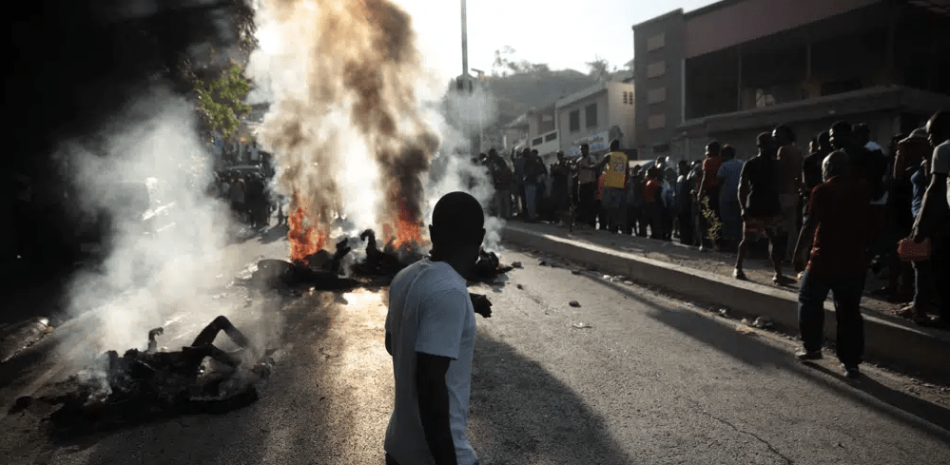 Un grupo de personas observa los cadáveres de presuntos pandilleros que fueron quemados vivos por una turba en la sección Canape Vert de Puerto Príncipe, Haití, el lunes 24 de abril de 2023. (AP Foto/Odelyn Joseph)