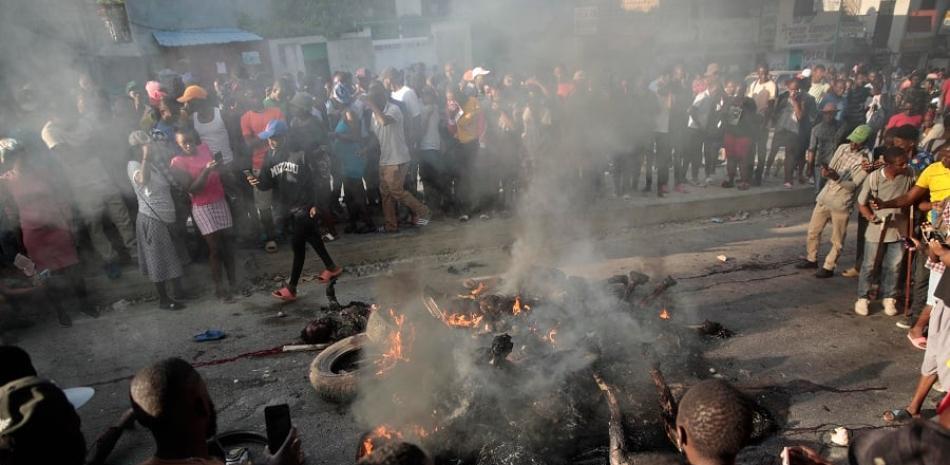 NOTA EDS: CONTENIDO GRÁFICO - Los transeúntes observan los cuerpos de los presuntos pandilleros que fueron incendiados por una turba después de que la policía los detuviera mientras viajaban en un vehículo en el área de Canape Vert de Port-au-Prince, Haití, el lunes. 24 de abril de 2023. (Foto AP/Odelyn Joseph)