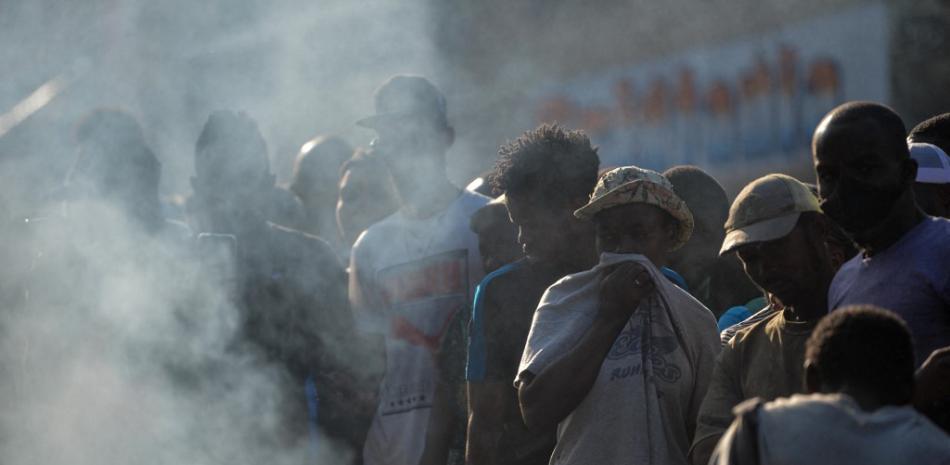 Personas miran cuerpos en la calle de miembros de bandas quemados en Puerto Príncipe.