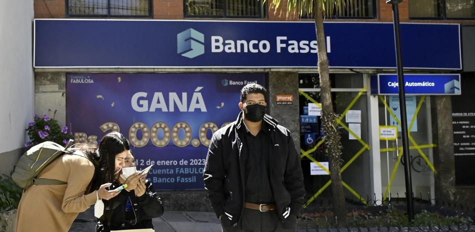 People walk past a branch of Fassil Bank, a day after Bolivia's government took control of the entity following the arrest of four of its executives for alleged mismanagement, in La Paz, on April 27, 2023. (Photo by Aizar RALDES / AFP)
