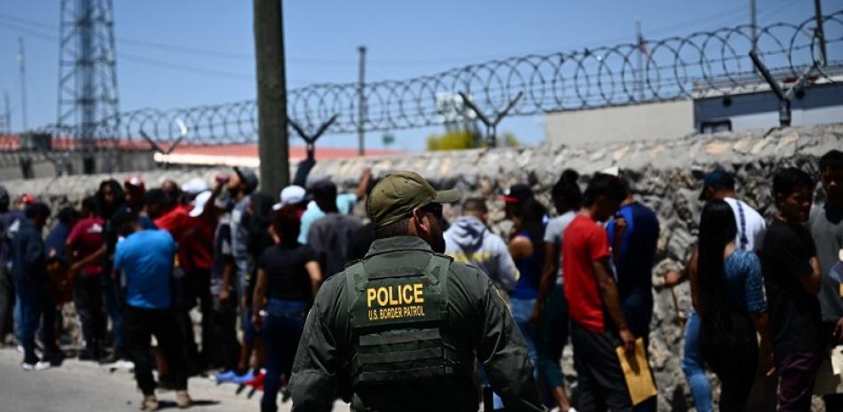 Un agente de la Patrulla Fronteriza camina a lo largo de una fila de migrantes que esperan entregarse a los agentes de la Patrulla Fronteriza de Aduanas y Protección Fronteriza de EE. UU. después de cruzar la frontera mexicana.