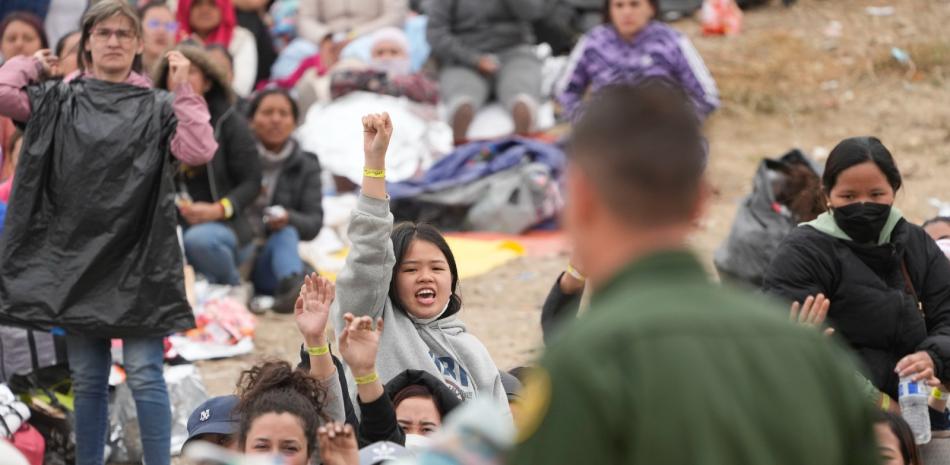 Las mujeres sostienen sus pulseras en alto con la esperanza de que los agentes de la Patrulla Fronteriza de EE. UU. las elijan para ser procesadas después de esperar días entre dos muros fronterizos para solicitar asilo.