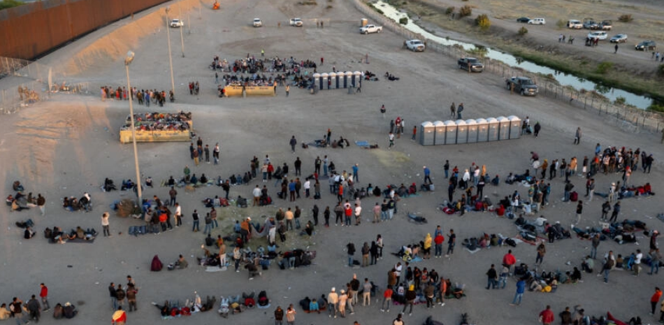 Migrantes esperan en el muro fronterizo para entrar a El Paso.