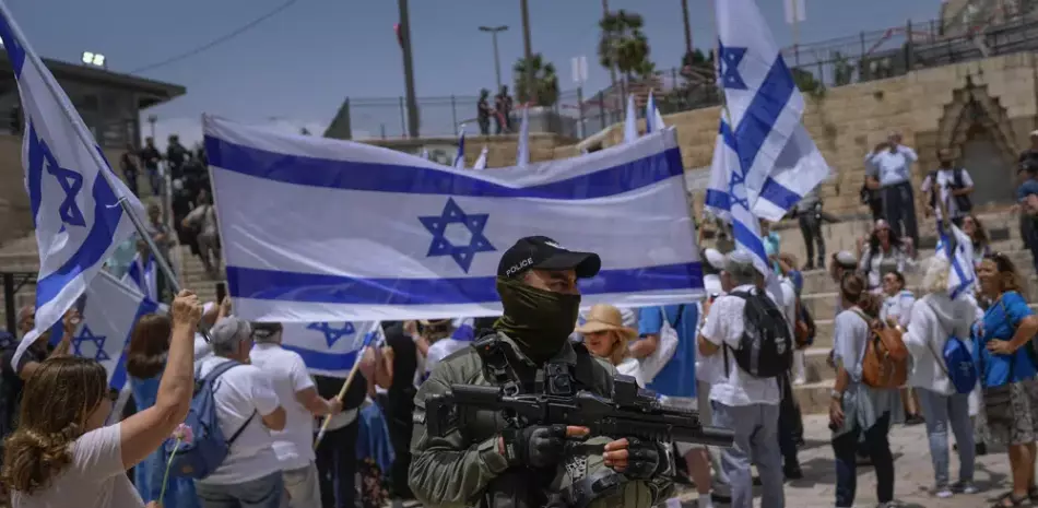 Un agente de la policía de Israel hace guardia mientras israelíes ondean banderas nacionales antes de una marcha por el Día de Jerusalén, ayer.