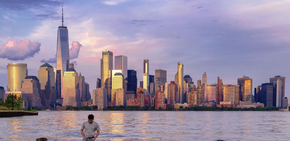 Un hombre comprueba dónde pisa mientras camina por el agua en el Canal Morris en Jersey, Nueva Jersey, mientras se pone el sol con Manhattan de fondo, el 31 de mayo de 2022.