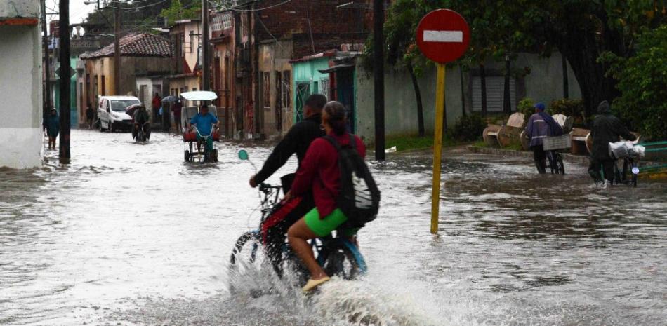 En esta fotografía difundida por ACN, personas pasean en motocicleta por una calle después de que las fuertes lluvias provocaran una inundación en Camagüey, Cuba, el 9 de junio de 2023.