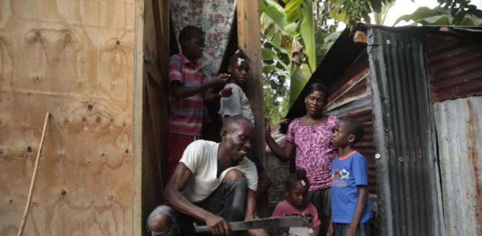 Mackenson Victor abre un coco para su hija, Manouchi Victor, el centro al frente, y sus hijastros, en su casa en una zona rural de Saint-Louis-du-Sud, Haití, el jueves 25 de mayo de 2023