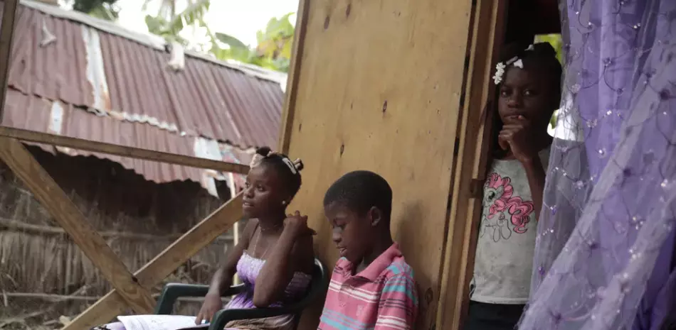 Los hermanos Mylouise Veillard, a la izquierda, y Myson estudian junto a su hermana Routcheland, de pie en la entrada de su casa en una zona rural de Saint-Louis-du-Sud, Haití, el jueves 25 de mayo de 2023.