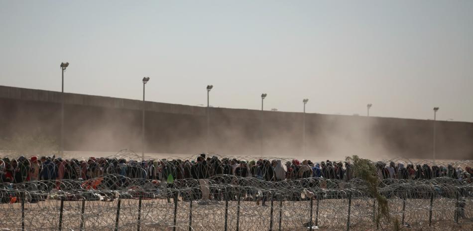 ARCHIVO - Migrantes alineados entre una valla con alambre de púas y el muro fronterizo entre Estados Unidos y México, visto desde Ciudad Juárez, México, el 9 de mayo de 2023.