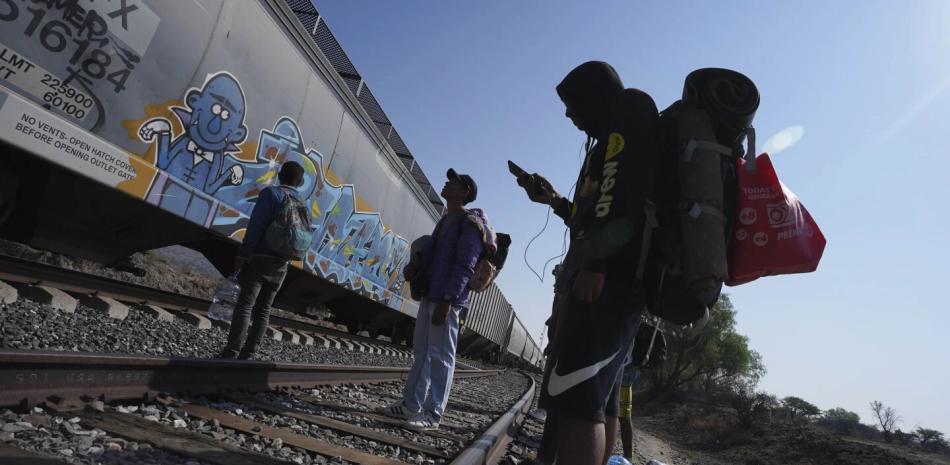 Migrantes ven pasar un tren mientras esperan a lo largo de las vías.
