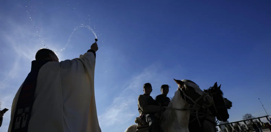 Un sacerdote bendice con agua bendita a jinetes durante celebración