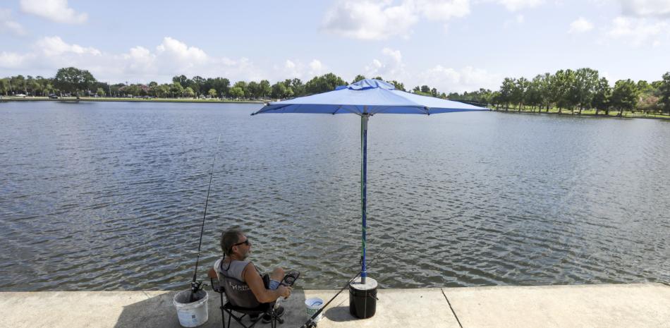 Lee Guidry pesca sentado bajo una sombrilla el martes 27 de junio de 2023, en Metairie, Luisiana.
