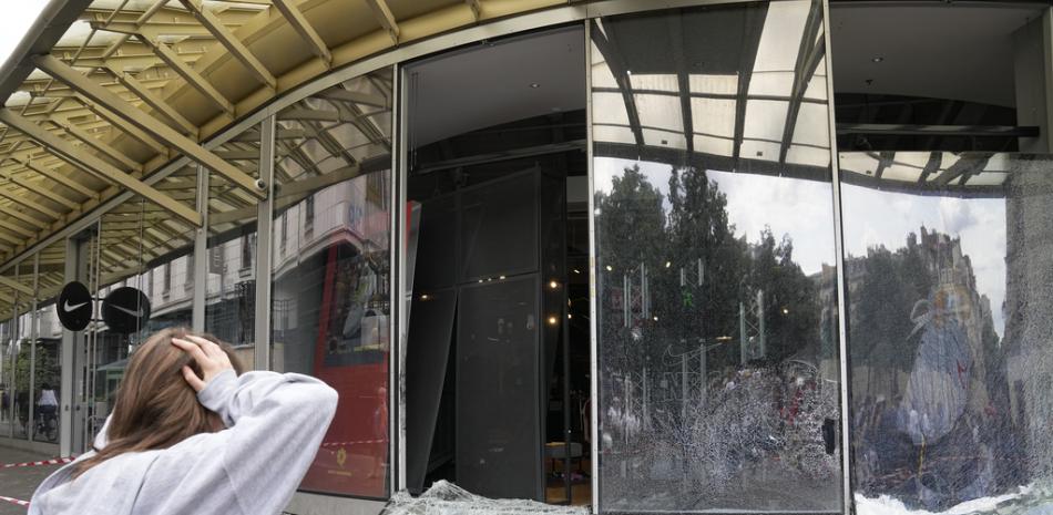 Una mujer reacciona frente a una tienda de deportes dañada después de una tercera noche de disturbios en Francia