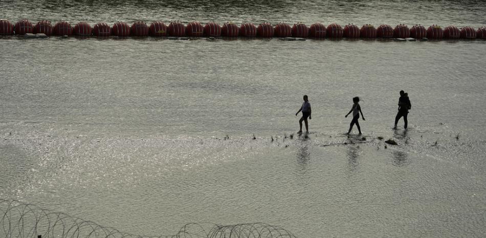 Migrantes pasan junto a grandes boyas que se utilizan como barrera fronteriza flotante en el Río Grande