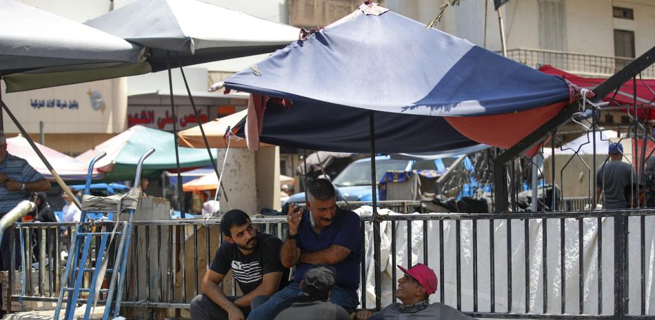 Trabajadores iraquíes se refrescan bajo un paraguas durante una ola de calor en el mercado de Shorja en el centro de Bagdad el 13 de agosto de 2023.