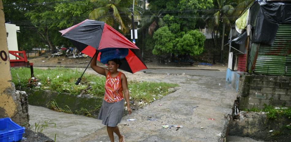 Comunitaria con sombrilla en mano camina por donde cruza la cañada en el barrio Las 800, en el sector Los Ríos, Distrito Nacional.
