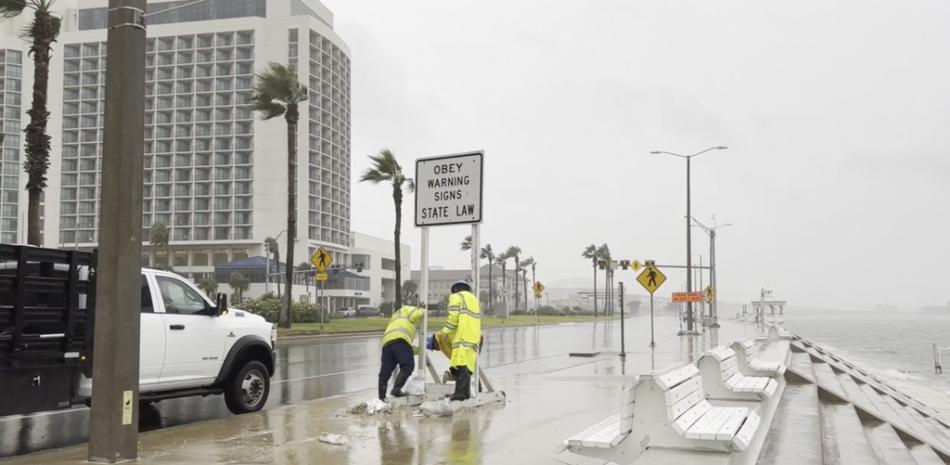 los trabajadores aseguran un letrero mientras soplan fuertes vientos de la tormenta tropical Harold