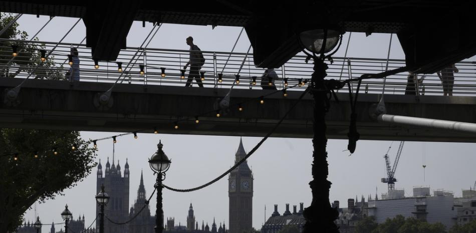 Un hombre camina sobre un puente con el fondo de las Casas del Parlamento durante un día soleado en Londres,