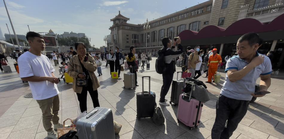 Viajeros con su equipaje esperan en una plaza de la estación de tren Beijing, en la capital de China, el viernes 29 de septiembre de 2023.