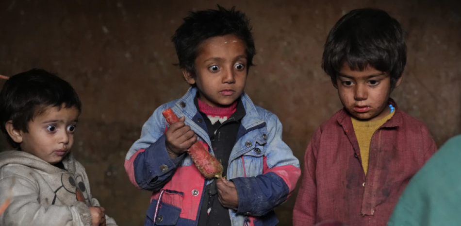 Tres niños desplazados miran con sorpresa la manzana que su madre pudo llevar a casa