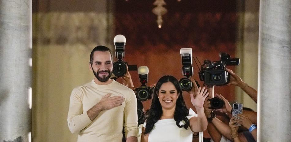 El presidente de El Salvador, Nayib Bukele, acompañado por su esposa Gabriela Rodríguez, saluda a sus seguidores desde el balcón del palacio presidencial.