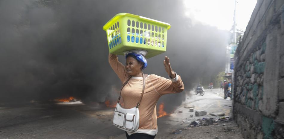 Una mujer corre junto a una barricada de neumáticos en llamas colocada por manifestantes contrarios al primer ministro, Ariel Henry, en Puerto Príncipe.