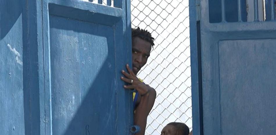 Esta captura de pantalla tomada de AFPTV muestra a una persona mirando desde detrás de una puerta cerca de la prisión principal de Puerto Príncipe, Haití