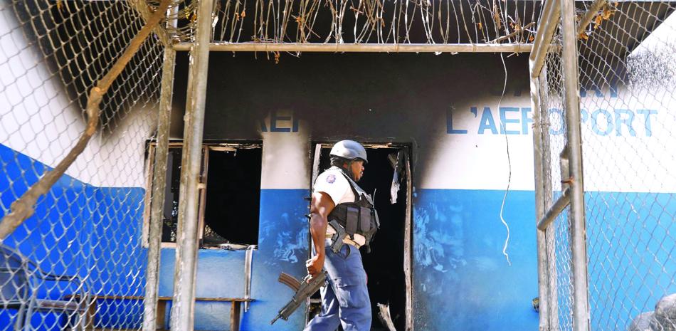 Un policía camina junto a una comisaría quemada que fue incendiada por pandilleros en Puerto Príncipe,  el martes 5 de marzo de 2024.