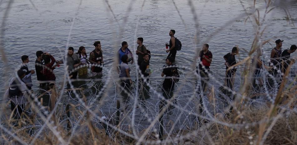 Migrantes esperan para trepar por encima del alambre de púas después de cruzar el Río Bravo y entrar en Estados Unidos desde México, el 23 de septiembre de 2023 en Eagle Pass, Texas.