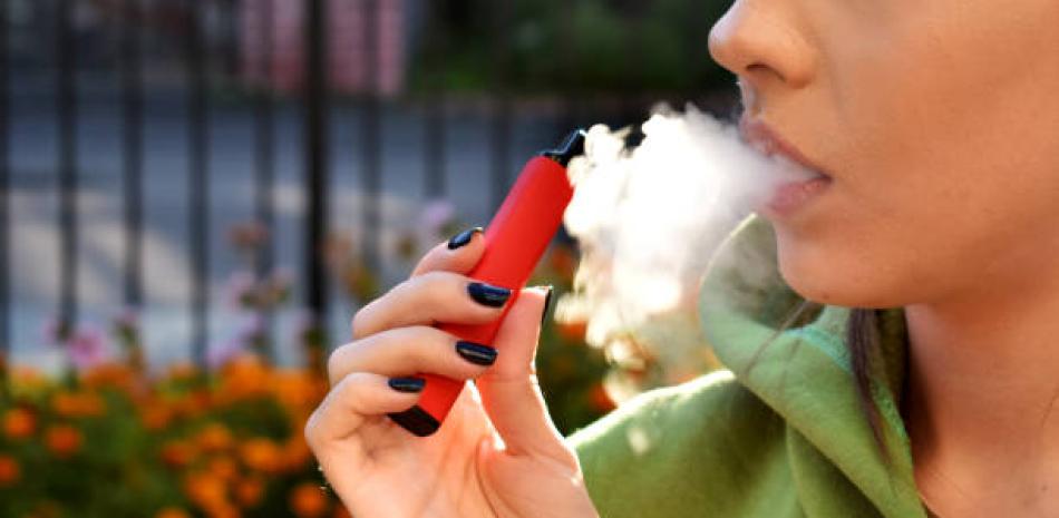 Fotografía muestra mujer fumando cigarrillo electrónico en lugar público.