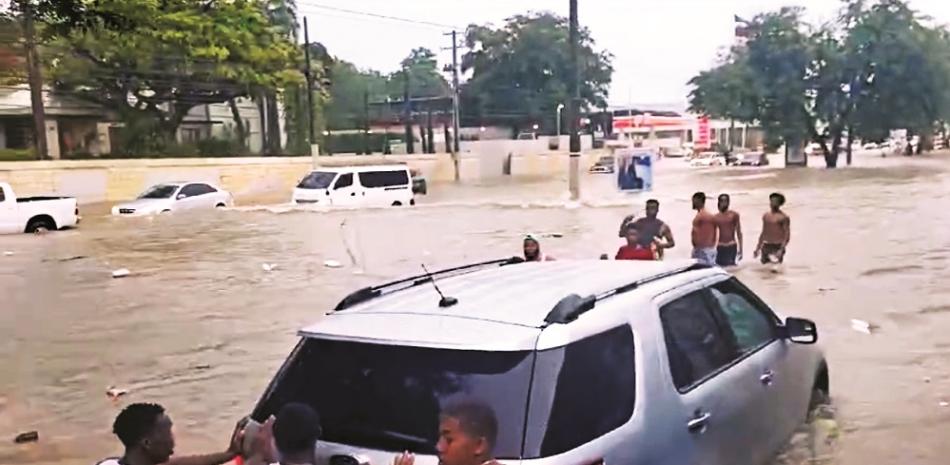 Estos jóvenes dan “una mano” al conductor de este vehículo, sacándolo de un atasque en un gran cúmulo de agua en una avenida de Santo Domingo.