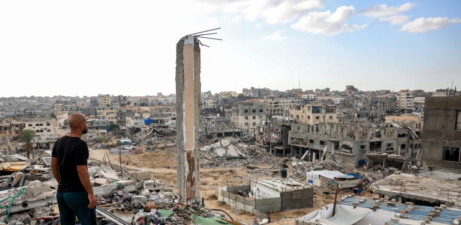 Un hombre parado en lo alto de un edificio muy dañado ve otros edificios destruidos en Khan Yunis, en el sur de la Franja de Gaza. Foto de Bashar TALEB