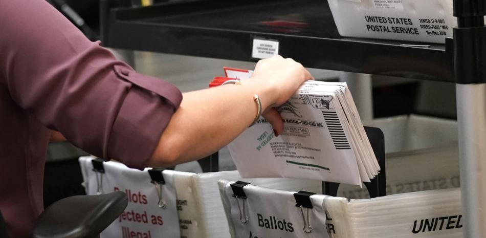 Un trabajador electoral con votos por correo en la mano en el centro electoral del condado de Miami-Dade, el lunes 26 de octubre de 2020, en Doral, Florida