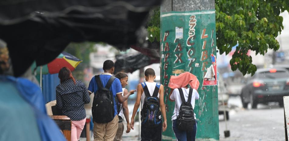 Estudiantes caminan bajo la lluvia en una acera del Distrito Nacional.