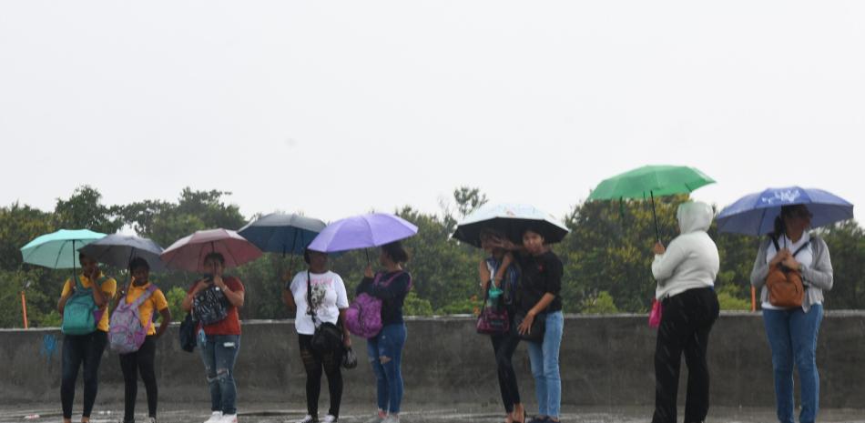 Varias personas se cubren de la lluvia con paraguas mientras esperan el transporte público.