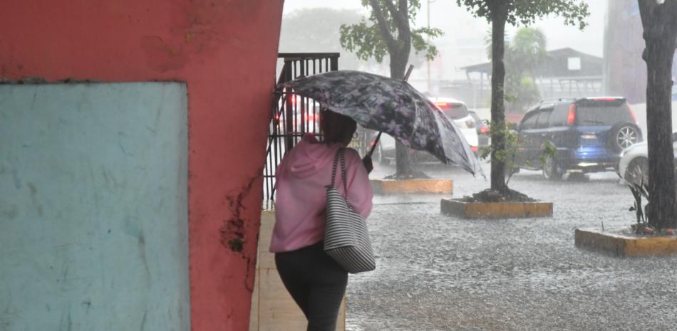 Una mujer se cubre de la lluvia mientras camina por una acera inundada de la capital.