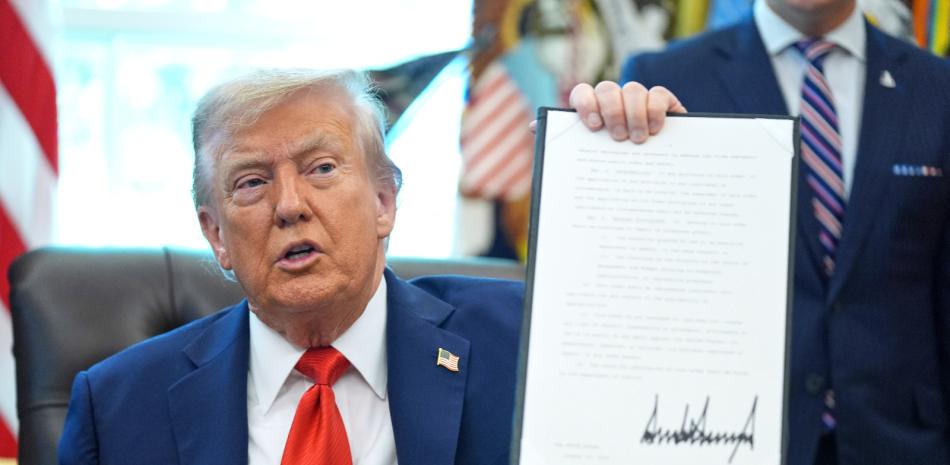 El presidente Donald Trump sostiene una orden ejecutiva firmada que requiere que el Departamento de Justicia investigue los casos de quema de banderas, en la Oficina Oval de la Casa Blanca, ayer.