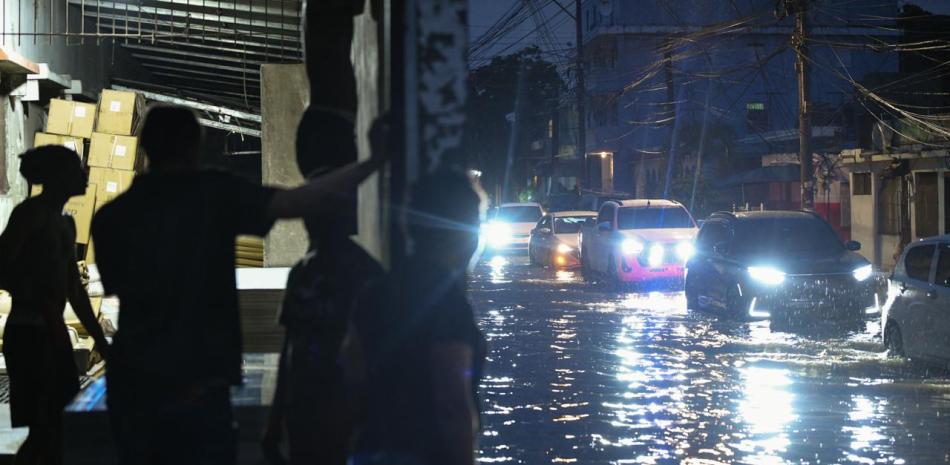 Personas se refugian de las inundaciones en un negocio, mientras varios vehículos se desplazan por una calle
