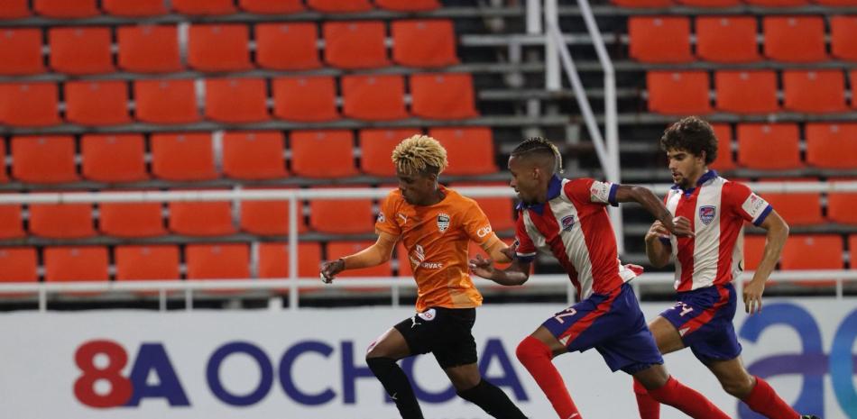 Yunior Peralta de Cibao FC perseguido por Isaac Corcino y Diego lOSADA de Delfines del Este