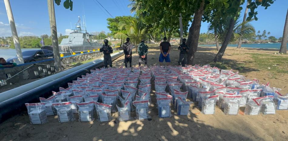 Imágen del cargamento decomisado de supuesta cocaína junto a los hombres que fueron arrestados por portarla en una narcolancha.